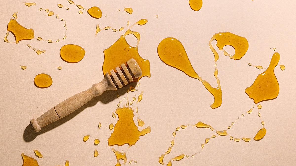 Wooden honey dipper with honey splashes on a beige background