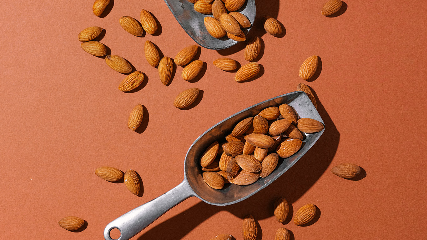 Almonds in a metal scoop on an orange background
