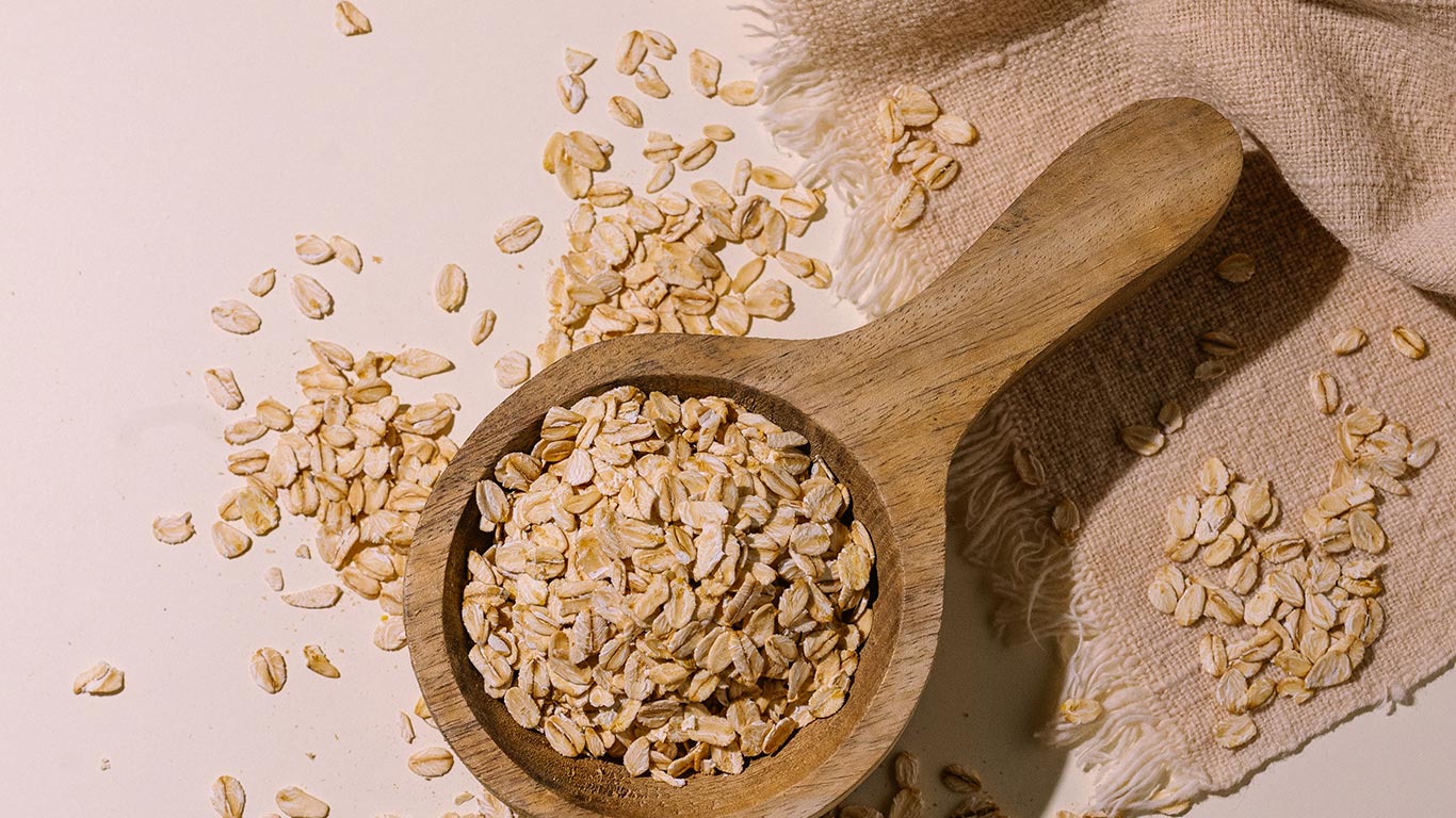 Wooden scoop filled with oats on a light background
