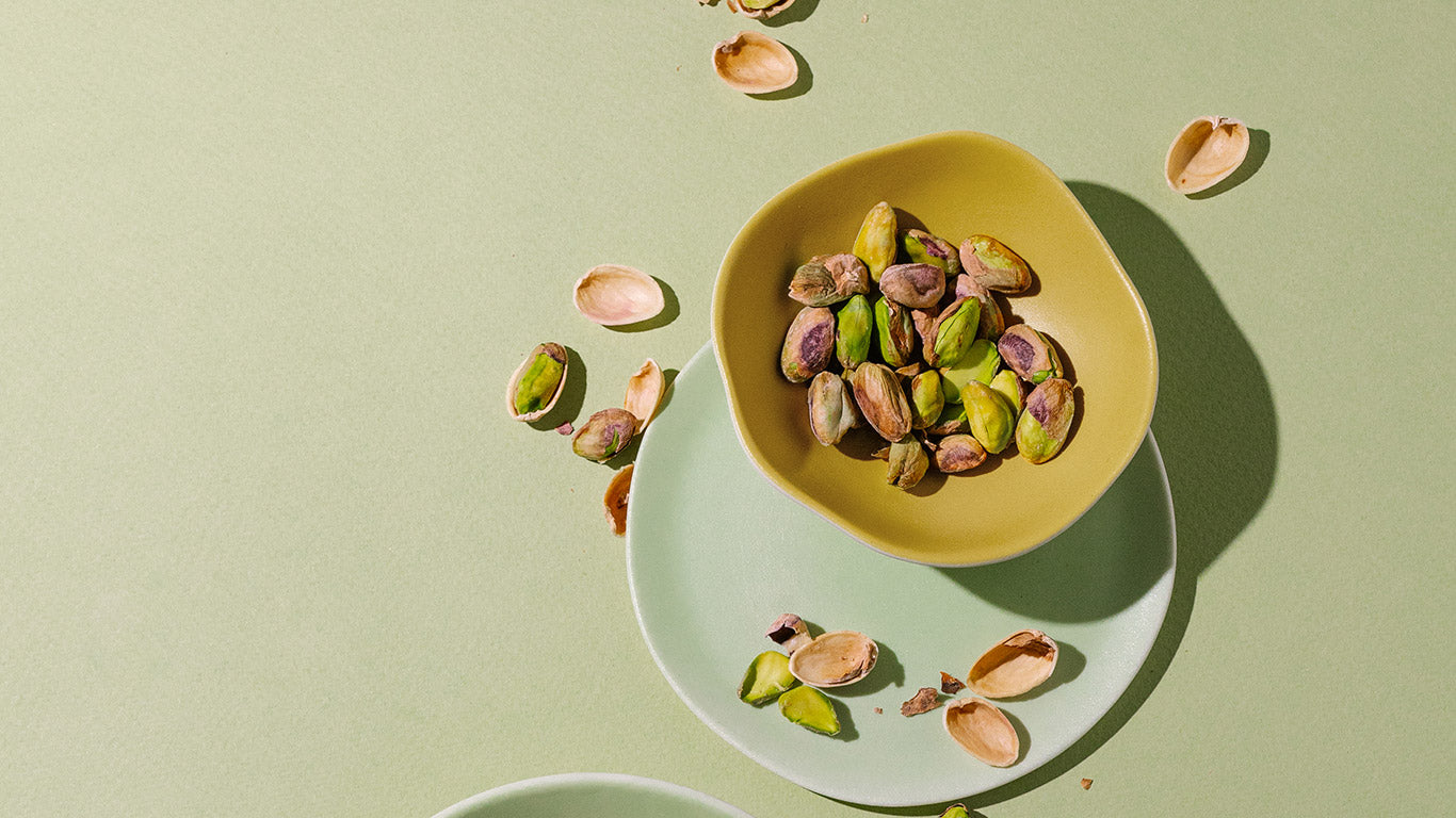 Yellow bowl filled with pistachios on a light green background