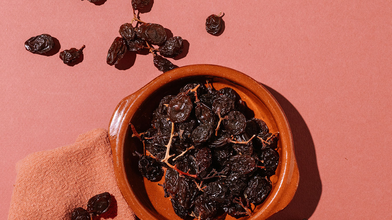 Terracotta bowl filled with dried fruits on a pink background